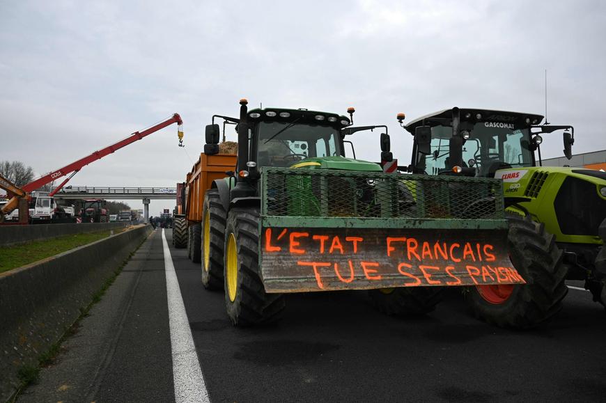 Un tracteur arborant le slogan « L'Etat français tue ses paysans » est garé le long de l'autoroute A64, lors d'un blocage organisé par des agriculteurs pour protester contre le protocole d'abattage obligatoire imposé par le gouvernement aux troupeaux de bovins touchés par la dermatose nodulaire contagieuse, à Carbonne (Haute-Garonne), le 19 décembre 2025.