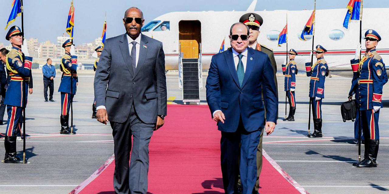 A handout picture released by the Egyptian Presidency shows Egyptian President Abdel Fattah al-Sisi (R) walk the red carpet as he greets Sudan's army chief General Abdel Fattah al-Burhan in Cairo on December 18, 2025. (Photo by Handout / Egyptian Presidency / AFP) / RESTRICTED TO EDITORIAL USE - MANDATORY CREDIT 