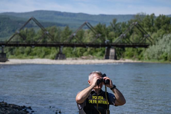 Un policier des frontières roumain inspecte les rives de la Tisza, avec en arrière-plan le pont de bois reliant la Roumanie et l’Ukraine, près du poste frontière de Sighetu Marmatiei (Roumanie), le 17&nbsp;mai 2024.
