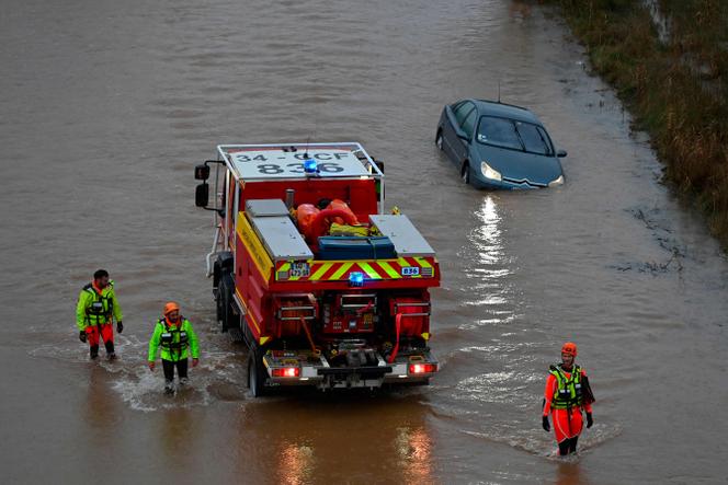 Des secouristes français passent devant une voiture près de la rivière Hérault, qui a débordé à la suite de fortes pluies à Agde, dans le sud de la France, le 23 décembre 2025.