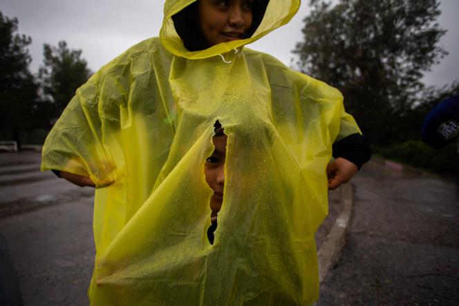 Un garçon regarde à travers un trou dans le poncho imperméable de sa mère, lors d’une ballade sous la pluie dans le parc Elysian, à Los Angeles, le 24 décembre 2025.