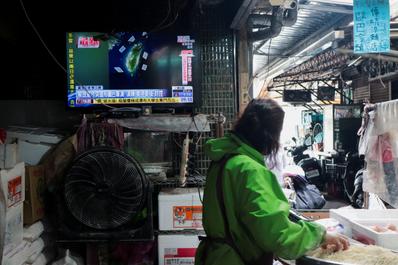 A woman works in a noodle store near a television screen showing a news report on China's 
