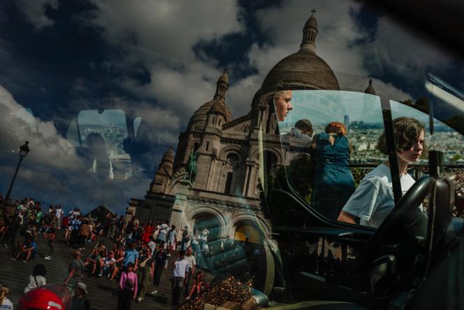 La basilique du Sacré-Cœur se reflète dans le pare-brise d’un taxi tandis que des touristes flânent sur la butte Montmartre à Paris, le 1er&nbsp;août&nbsp;2025.