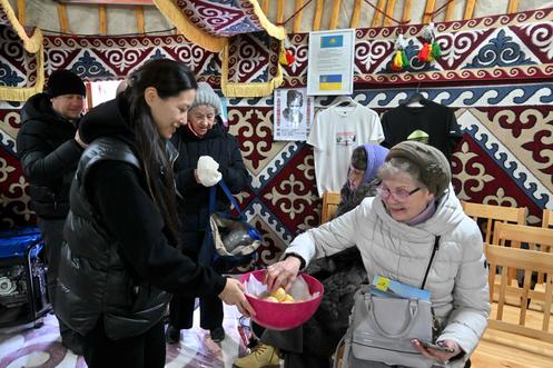 Une bénévole offre du pain traditionnel kazakh à des personnes venues profiter de l’occasion pour se réchauffer et recharger leurs appareils électroniques, dans une yourte installée dans un parc, à Kiev, le 10 janvier 2026.
