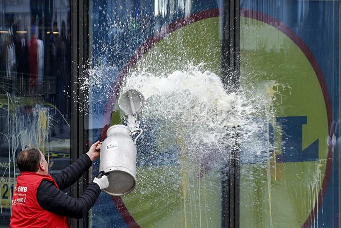 Un agriculteur déverse un seau de lait sur la vitrine du siège de Lidl, lors d’une manifestation, à Châtenay-Malabry (Hauts-de-Seine), le 15 janvier 2026.