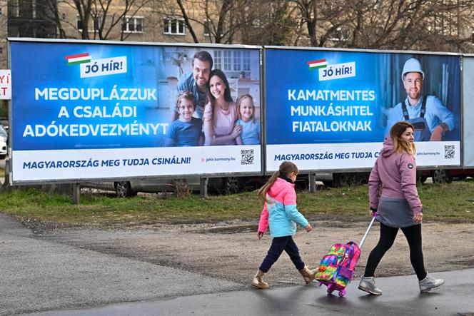 Devant des panneaux annonçant des mesures économiques prises par le gouvernement hongrois, dont celui, à gauche, qui affiche le message&nbsp;: «&nbsp;Nous avons doublé les allocations familiales.&nbsp;» A Budapest, le 28&nbsp;janvier&nbsp;2025. 