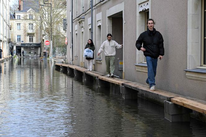 Des piétons marchent sur des passerelles improvisées dans une rue inondée après les fortes pluies qui ont provoqué le débordement de la rivière Maine à Anger, le 20&nbsp;février 2026.