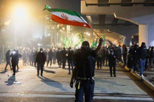 Um manifestante agita uma bandeira iraniana enquanto apoiadores de grupos armados xiitas iraquianos tentam marchar em direção à Embaixada dos EUA na Zona Verde de Bagdá, em 1º de março de 2026.