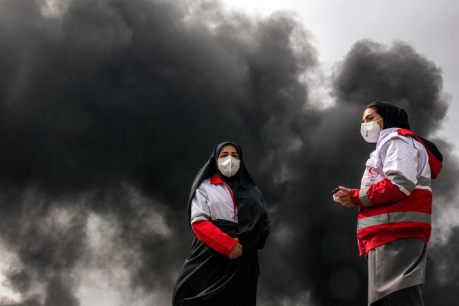 Women members of Iran's Red Crescent society stand near smoke plumes from an ongoing fire following an overnight airstrike on the Shahran oil refinery in northwestern Tehran on March 8, 2026.