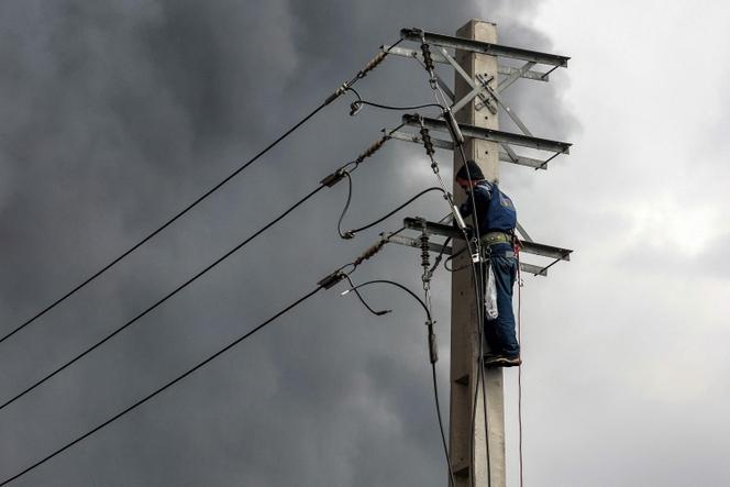 A technician repairs a power line before a cloud of smoke from a nearby ongoing fire following an overnight airstrike on the Shahran oil refinery in northwestern Tehran on March 8, 2026.