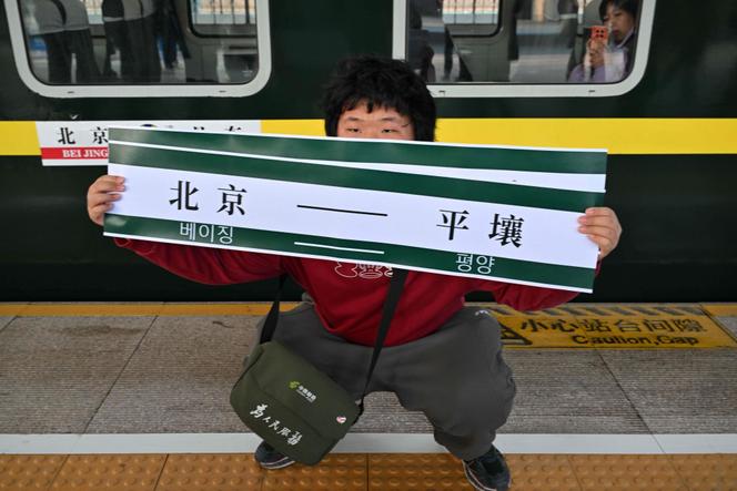 Un homme brandit une banderole sur laquelle on peut lire « Pékin-Pyongyang » devant le train K27 à destination de Pyongyang, en gare de Pékin, le 12 mars 2026.