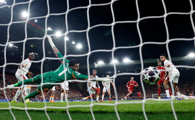 Dominik Szoboszlai, do Liverpool (fundo, vermelho), marca o primeiro gol de seu time contra Ugurcan Cakir, do Galatasaray. No estádio Anfield, Liverpool, 18 de março de 2026.