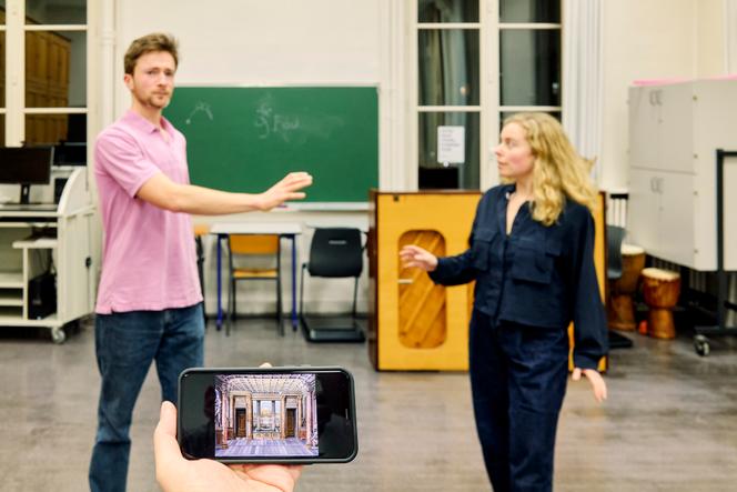 Répétition de la pièce « L’Astrologue ou les Faux Présages », à Paris, le 27 février. Le metteur en scène Mickaël Bouffard tient son téléphone avec les décors produits par IA devant les comédiens Mathieu Menant et Léa Sorrentino.