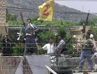 Appollaiati sulla cima di un carro armato T-55 abbandonato dall'esercito del Libano del Sud a Kfar Kila (Libano), alcuni fedayn brandiscono un poster dello sceicco Hassan Nasrallah, leader di Hezbollah, il 24 maggio 2000.