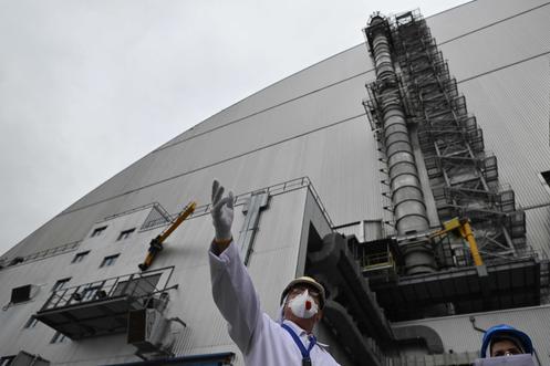 Oleksandr Skomarokhov (à esquerda), vice-diretor técnico da usina nuclear de Chernobyl encarregado da gestão de resíduos radioativos, em frente ao novo arco de contenção, uma cúpula de metal que cobre o sarcófago do quarto reator destruído da usina, 9 de abril de 2026.