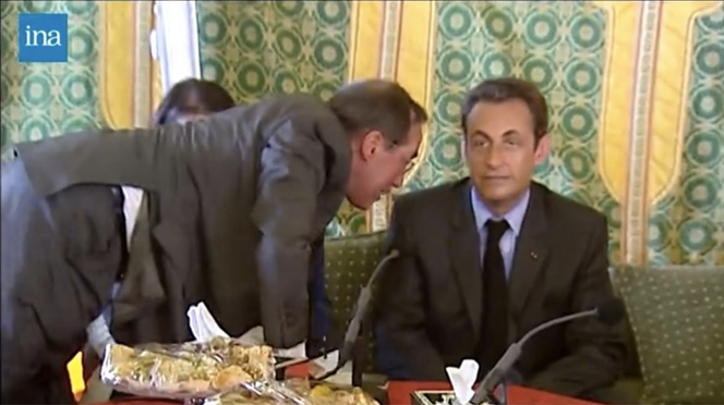 Captura de tela do documentário “O Presidente e o Ditador” de Antoine Vitkine, onde Claude Guéant sussurra no ouvido de Nicolas Sarkozy, em Trípoli (Líbia), 25 de julho de 2007, durante a refeição oficial organizada por Muammar Gaddafi.