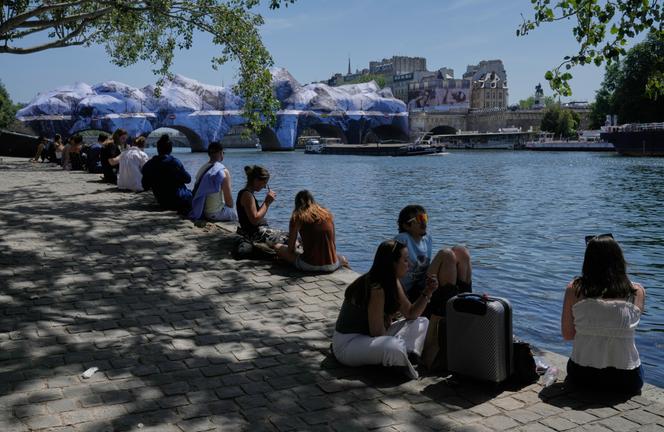 People seek relief from the heat along the Seine River in Paris, Monday, May 25, 2026. Artwork by street artist JR is seen on the Pont Neuf in the background.
