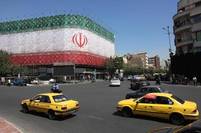 Traffic moves past the Iranian national flag displayed on a building at Enghelab square in Tehran on June 14, 2026. 