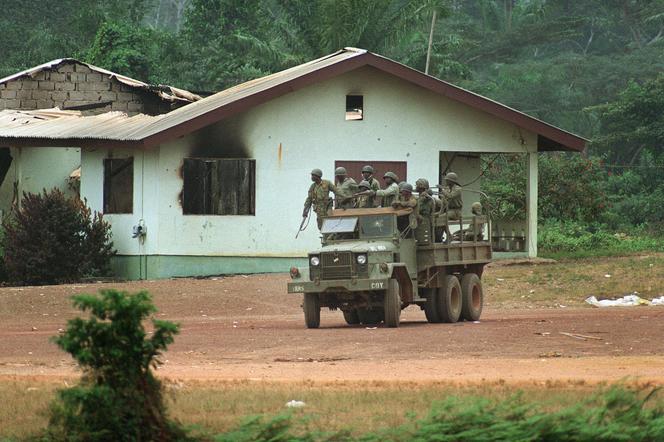 Un camion des Forces armées du Liberia (AFL) passe devant une maison incendiée par les rebelles du Front national patriotique du Liberia (NPFL) dans le village frontalier de Logatuo, Le 13 janvier 1990. - PASCAL GUYOT/AFP