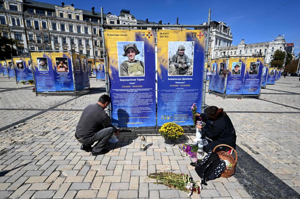 Des personnes déposent des fleurs devant les portraits de leurs proches, des combattants de la brigade Azov morts au combat, qui ont été installés sur la place Sainte-Sophie, dans le centre de Kiev, le 15 septembre 2026. - SERGEI SUPINSKY/AFP