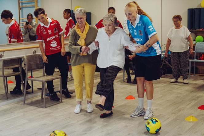 Les joueuses Héléna Theriez (maillot rouge) et Marie Percebois (en bleu) avec les résidentes Maryse Frys (en jaune) et Camille Moitel (au centre), pendant le cours de sport à la résidence Les Bénédictines, à Tourcoing (Nord), le 23 septembre 2026. - AIMÉE THIRION POUR M LE MAGAZINE DU MONDE