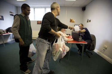 Volunteers handing over provisions bags at the Stoke Food Bank at the Hanley Baptist Church in Stoke-on-Trent, England. The food bank caters for about 50 people each week by supplying people with basic food items and was typical of many in existence in England during the recession. The UK government were to announce their latest spending round the following day, with many communities expected to face further hardship.