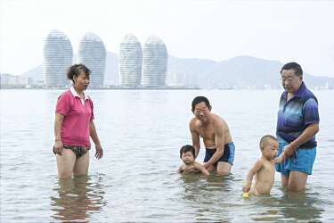 Une famille savoure les joies de la  baignade devant  les tours en construction de Phoenix Island. Hainan est réputée pour la qualité de ses eaux, les seules de Chine épargnées par la pollution. -