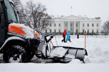 A plow removes snow from the sidewalk in Lafayette Park across the street from the White House in Washington, Thursday, Feb. 13, 2014, as people walk through the snow. After pummeling wide swaths of the South, a winter storm dumped nearly a foot of snow in Washington as it marched Northeast and threatened more power outages, traffic headaches and widespread closures for millions of residents. (AP Photo/Jacquelyn Martin)