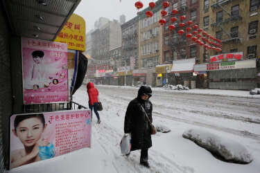Pedestrians walk along a snow-covered sidewalk in the Chinatown neighborhood of New York, Thursday, Feb. 13, 2014. Snow and sleet are falling on the East Coast, from North Carolina to New England, a day after sleet, snow and ice bombarded the Southeast. (AP Photo/Mark Lennihan)