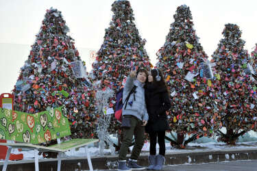 In a picture taken on December 10, 2012, a couple take pictures in front of trees made by "locks of love" at a terrace of the N Seoul Tower on the top of Nam mountain in Seoul. Young couples hang their "locks of love" and throw the key away in the hope for eternal love.    AFP PHOTO / JUNG YEON-JE