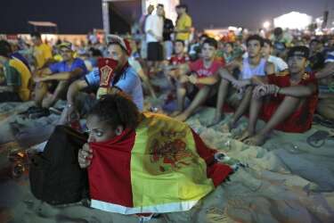 Wrapped in a Spanish national flag, a soccer fan watches the live broadcast of the World Cup match between Spain and the Netherlands inside the FIFA Fan Fest area on Copacabana beach in Rio de Janeiro, Brazil, Friday, June 13, 2014. The Netherlands thrashed Spain 5-1 Friday. It was a humiliating defeat for the defending World Cup champions. (AP Photo/Leo Correa)
