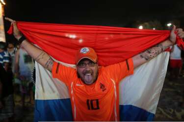 A soccer fan holding a Dutch national flag poses for a photo after watching the live broadcast of the World Cup match between Spain and the Netherlands, inside the FIFA Fan Fest area on Copacabana beach in Rio de Janeiro, Brazil, Friday, June 13, 2014. The Netherlands thrashed Spain 5-1 Friday. It was a humiliating defeat for the defending World Cup champions. (AP Photo/Leo Correa)