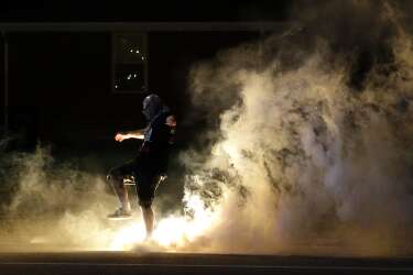A protester kicks a smoke grenade that had been deployed by police back in the direction of police Wednesday, Aug. 13, 2014, in Ferguson, Mo. Protests in the St. Louis suburb rocked by racial unrest since a white police officer shot an unarmed black teenager to death turned violent Wednesday night, with people lobbing Molotov cocktails at police who responded with smoke bombs and tear gas to disperse the crowd. (AP Photo/Jeff Roberson)