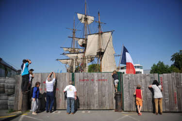 Curious check out from behind a fence as crew members hoist the sails of the replica of French frigate Hermione during a ceremony in Rochefort, western France, on May 17, 2014. The original Hermione was a 12-pounder Concorde class frigate of the French Navy, which in 1780 ferried General Lafayette to the United States to allow him to rejoin the American side in the American Revolutionary War. The replica is to set sail for a transatlantic crossing in 2015. AFP PHOTO / PHOTO XAVIER LEOTY