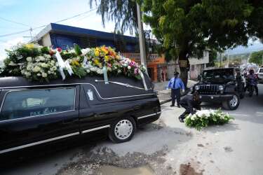 A man takes the flowers that fell while the coffin of former Haitian dictator Jean-Claude Duvalier is transported after a Mass at the chapel of the Saint-Louis Gonzague school, in Port-au-Prince on October 11, 2014, to the Pax-Villa Funeral Home. Duvalier, who died last week at age 63, was not granted a state funeral, his lawyer said October 9, after public outrage that a man accused of corruption and mass killings could receive such an honor. The Duvalier family lawyer, Reynold George, expressed bitterness that the government, "rather than stand by its principles, has ceded to pressure from certain figures." AFP PHOTO/Hector RETAMAL
