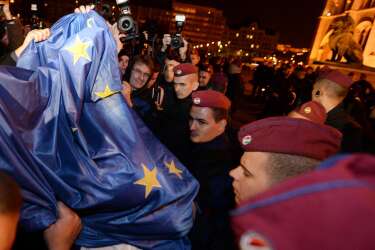 Participants of an anti-government demonstration lift an EU-flag in front of Hungarian policemen to display it on the parliament building in downtown Budapest on October 28, 2014 after their rally against the goverment's new tax plan for the introduction of the internet tax next year. Thousands of Hungarians marched in Budapest late Tuesday against a proposed law to tax Internet usage, in the second mass protest this week opposing the measure championed by Prime Minister Viktor Orban. AFP PHOTO / ATTILA KISBENEDEK